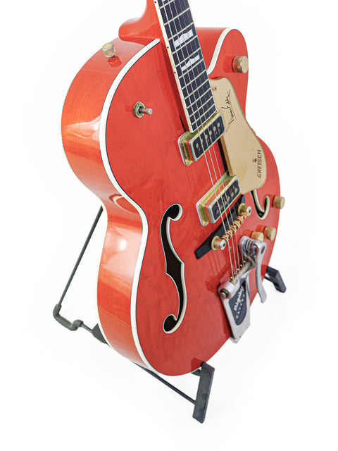 A striking red Gretsch 6120DE Duane Eddy Signature guitar displayed on a black stand, highlighting its unique features.