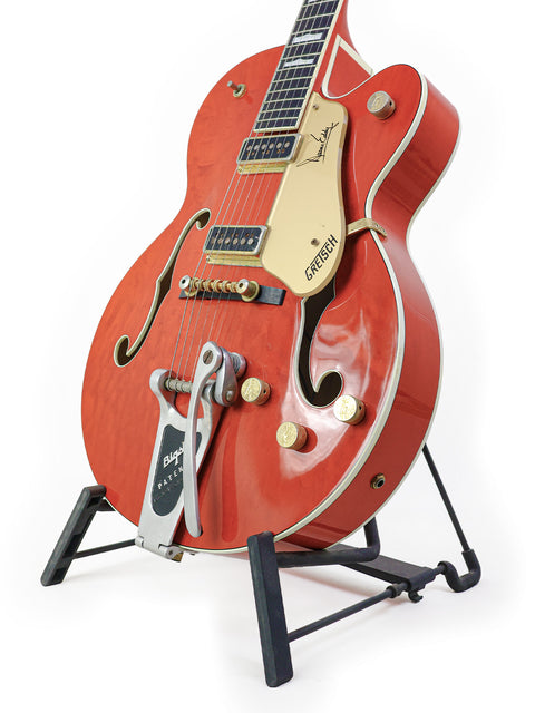 A striking red Gretsch 6120DE Duane Eddy Signature guitar displayed on a stand, set against a clean white backdrop.