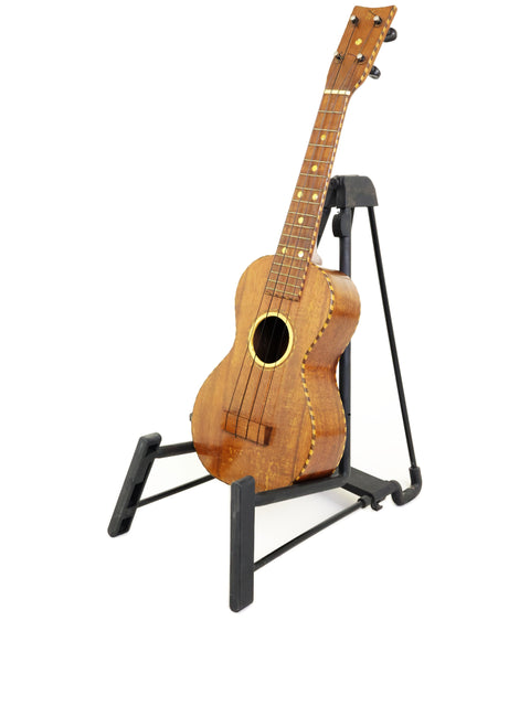A stunning Weissenborn Miami Style 3 Koa ukulele from 1924 rests on a stand, emphasizing its vintage elegance and artistry.
