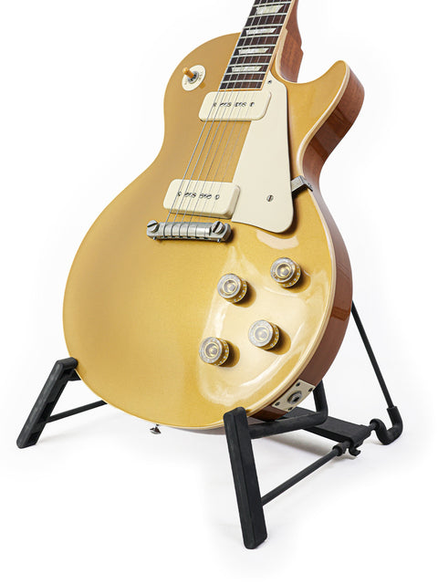A stunning gold Gibson Les Paul LPR-4 1954 Reissue guitar rests on a stand, set against a bright white backdrop.
