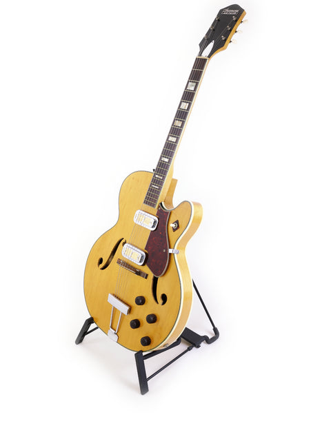 A stunning yellow Harmony H71 Meteor guitar on a stand, perfect for musicians seeking vintage charm against a clean white backdrop.