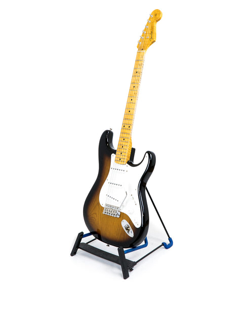 A sunburst electric guitar on a stand against a white background.