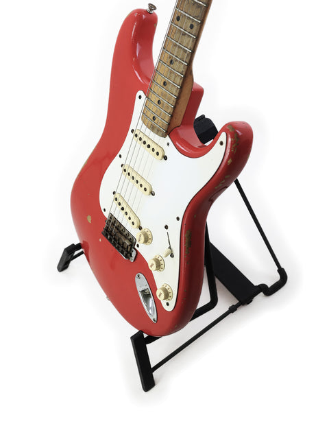 A vibrant red 1958 Fender Stratocaster guitar on a stand, contrasting against a simple white background, emphasizing its vintage appeal.