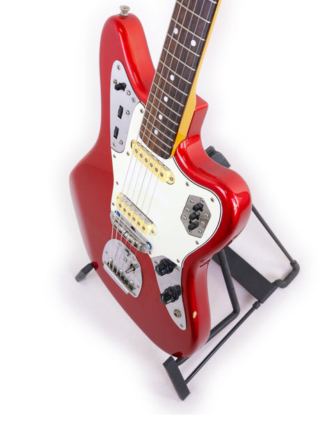 A vibrant red Fender CIJ Jaguar guitar resting on a stand, with a simple white backdrop that enhances its bold appearance.