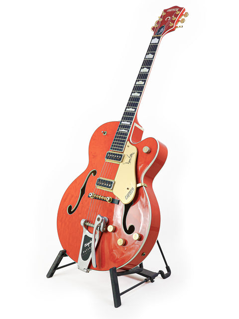 A vibrant red Gretsch 6120DE Duane Eddy guitar displayed on a stand with a clean white backdrop.