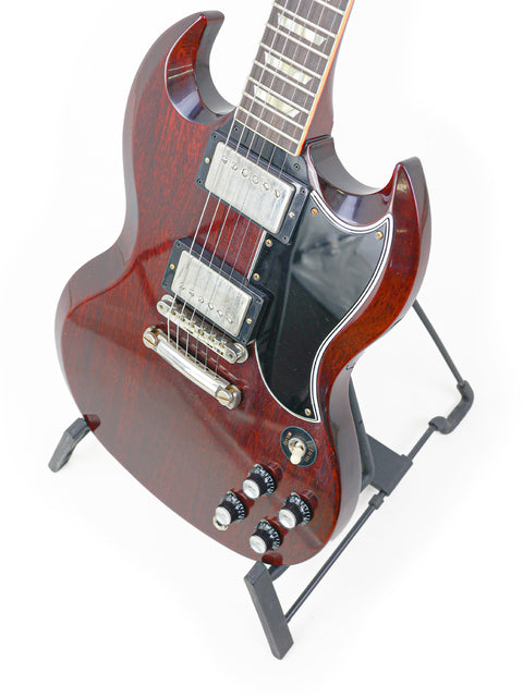 A vibrant red electric guitar displayed on a sleek black stand, featuring the Gibson Custom Shop '64 SG Standard 'CME Spec' from 2020.