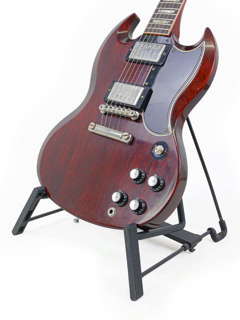 A vibrant red electric guitar, the Gibson Custom Shop '64 SG Standard, resting on a stand, highlighting its classic design.