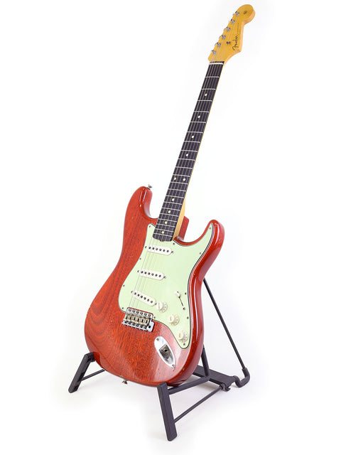  A vibrant red guitar on a stand, featuring the 2019 Fender Custom Shop Stratocaster design, with a simple white background.
