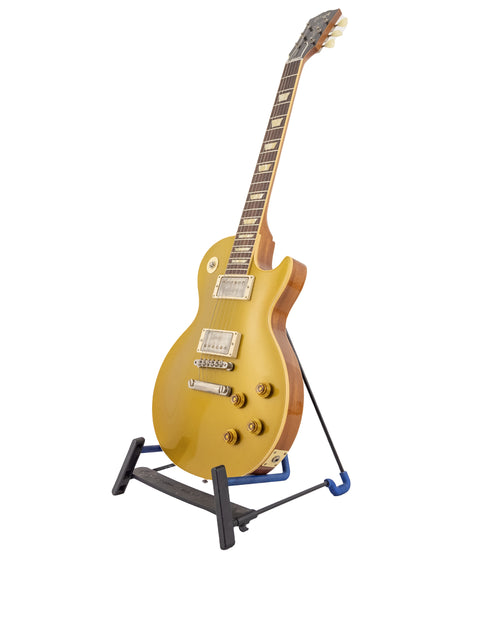 A vibrant yellow Gibson Custom Shop LPR-7 guitar displayed on a black stand, highlighting its classic 1957 Les Paul Goldtop style.