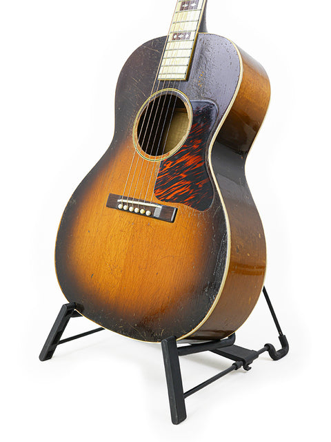 A vintage 1936 Gibson L-C 'Century of Progress' guitar displayed on a stand with a simple white backdrop.