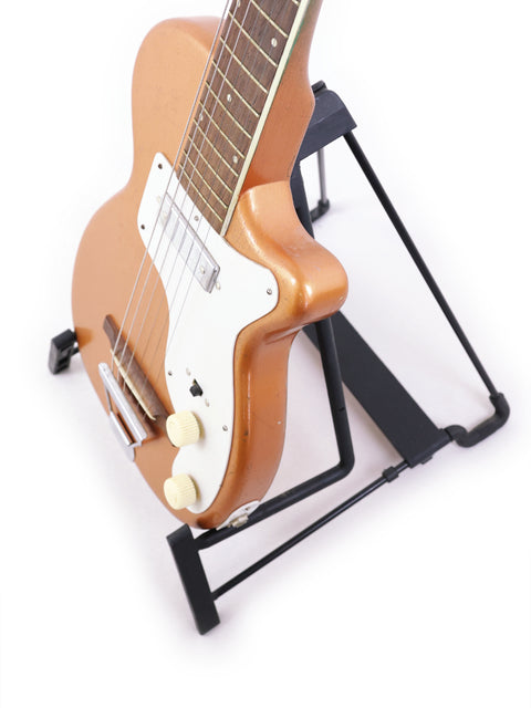 A vintage 1955 Harmony H44 Stratotone guitar resting on a stand with a plain white backdrop.