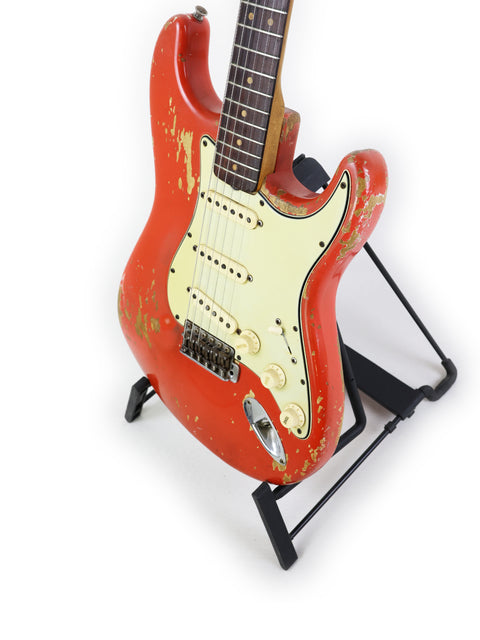 A vintage 1964 Fender L Series Stratocaster in Fiesta Red, displayed on a black stand against a white background.