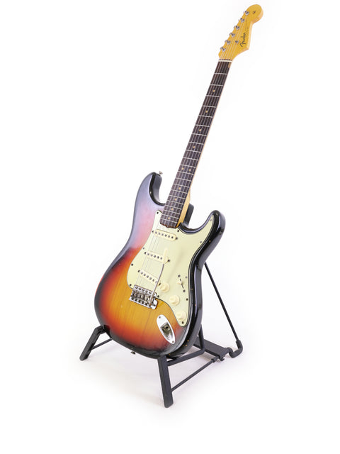 A vintage 1964 Fender L Series Stratocaster on a stand, showcasing its beauty against a white backdrop.