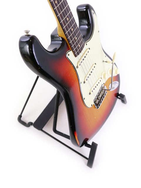 A vintage 1964 Fender L Series Stratocaster on a stand, showcasing its beauty against a white background.