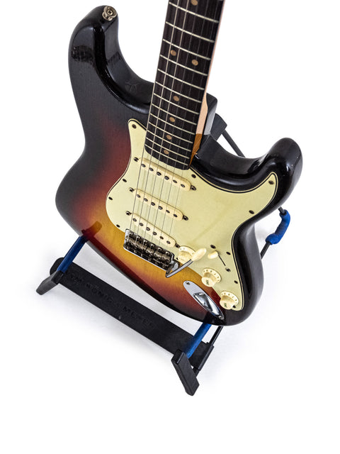 A vintage 1964 Fender Stratocaster in Fiesta Red, resting on a stand, showcasing its black pick guard.

