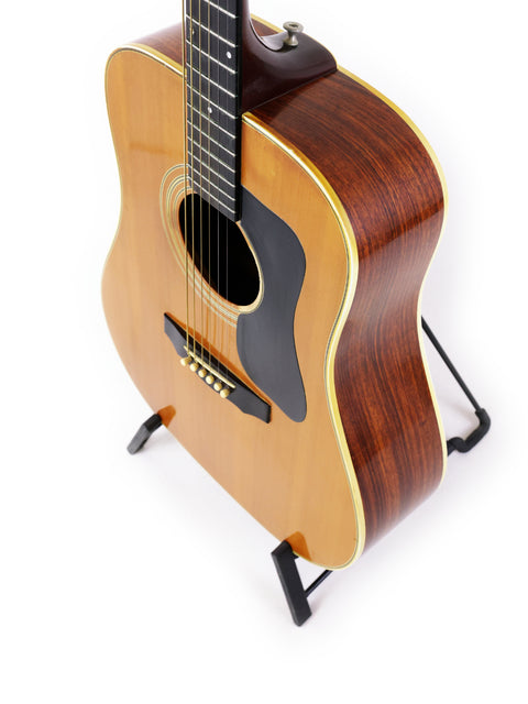 A vintage 1974 Guild D-50 Bluegrass Special guitar displayed on a stand with a white backdrop.