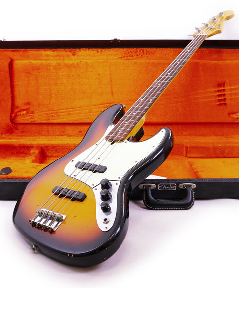 A vintage Fender Custom Shop '64 Jazz Bass guitar displayed in a case, emphasizing its relic features and classic style.