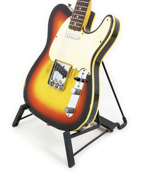 A vintage Fender Custom Telecaster from 1966, featuring a striking yellow and orange finish, resting on a stand.