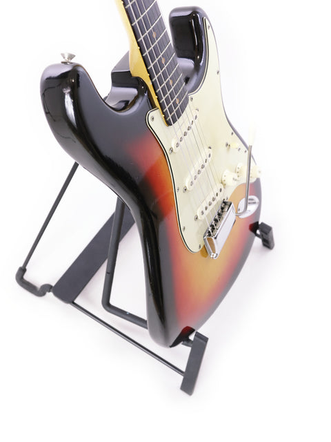 A vintage Fiesta Red Fender L Series Stratocaster guitar from 1964 showcased on a stand with a white background.

