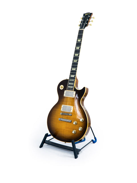 A vintage Gibson Les Paul guitar displayed on a stand, set against a stark white backdrop.