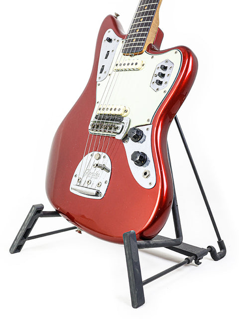 A vintage red L-Series Fender Jaguar guitar from 1964 elegantly positioned on a stand, emphasizing its refinished craftsmanship.