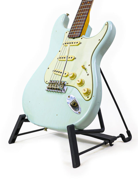 A white Fender Custom Shop '59 Stratocaster guitar on a black stand, showcasing its elegant design and craftsmanship.