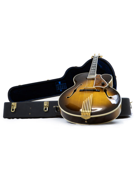 A white background highlights a Gibson Custom Shop Le Grand Archtop guitar and its case from 1997, emphasizing their beauty.
