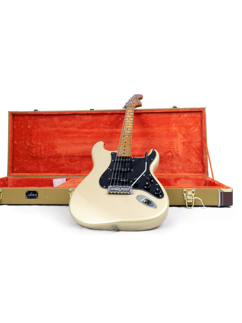 A white guitar, the Fender 25th Anniversary Stratocaster from 1979, resting in a striking orange case, emphasizing its vintage appeal.
