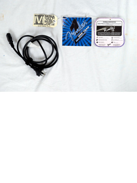 A white shirt featuring a black cord and a blue sticker, alongside a Fender Rumble 15 V3 Bass Combo Amp from 2019.