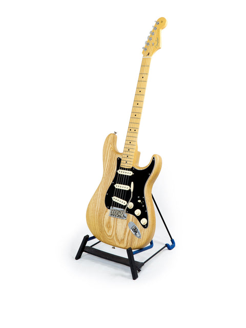A wooden Fender Stratocaster guitar displayed on a stand, featuring a natural oiled ash finish with a white backdrop.