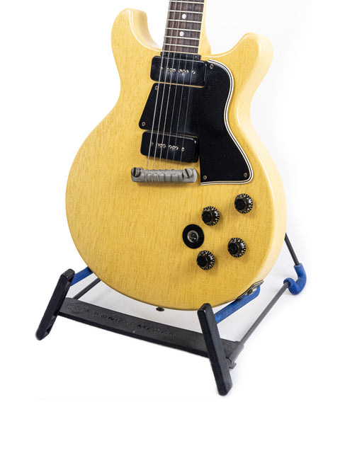 A yellow 1958 Gibson Les Paul Special guitar is displayed on a stand, highlighting its vintage charm and craftsmanship.