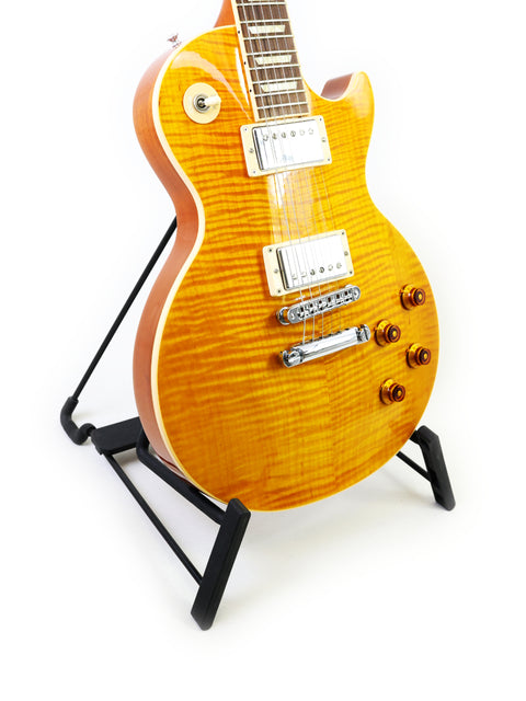 A yellow Gibson Les Paul Standard guitar sits on a guitar stand, emphasizing its striking color and iconic design from 2013.
