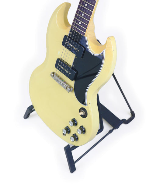 A yellow electric guitar, the Gibson Custom ‘63 SG Special, prominently featured on a stand, ready for performance.
