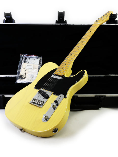 A yellow electric guitar with a maple neck leaning against an open case.