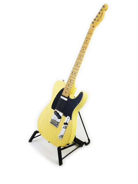 A yellow electric guitar with a maple neck on a black stand against a white background.