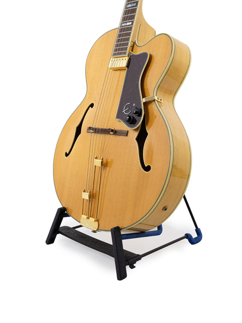 An Epiphone Coronet guitar from 1965 displayed on a stand with a plain white backdrop.