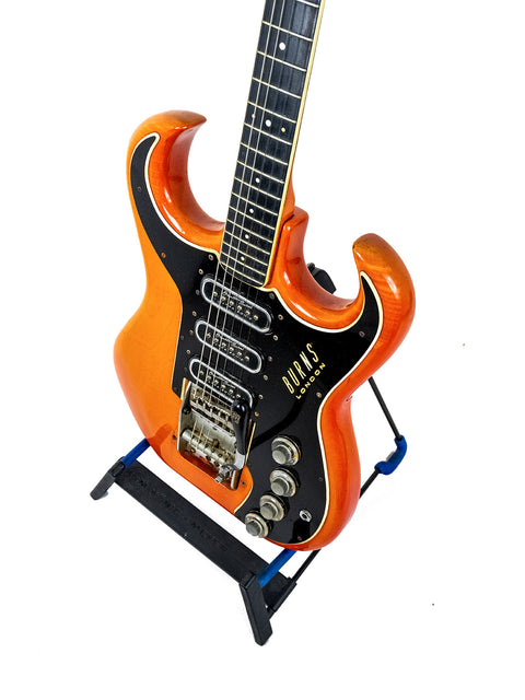 An eye-catching orange guitar displayed on a stand with a blue base, featuring the Warmoth Strat Partscaster from the USA.