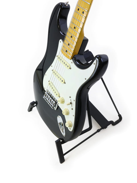 Black 1981 Fender Stratocaster guitar on a stand, showcasing its vintage charm against a bright white backdrop.