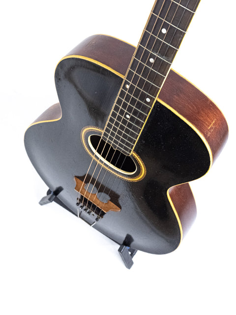 Black acoustic guitar, a vintage Gibson Style O from 1907, elegantly positioned on a wooden stand.