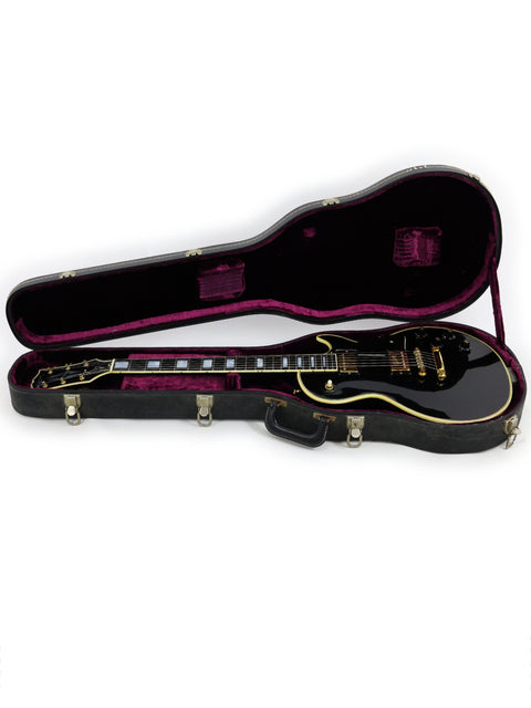 Black guitar case with purple lining, housing a vintage 1972 Gibson Les Paul Custom, a classic American instrument.