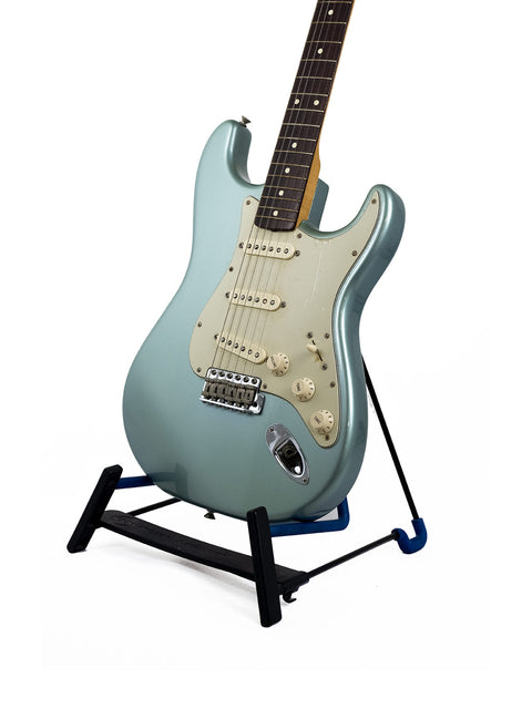 Blue electric guitar on a black stand against a white background.