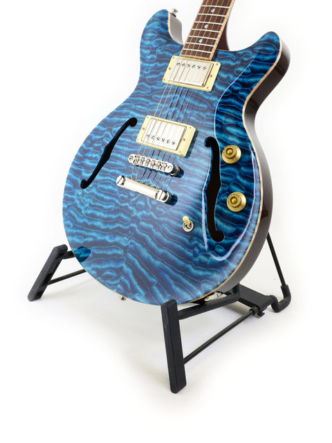 Blue electric guitar with wavy pattern on a stand against white background.