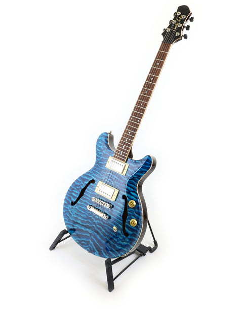 Blue electric guitar with wavy pattern on stand against white background.