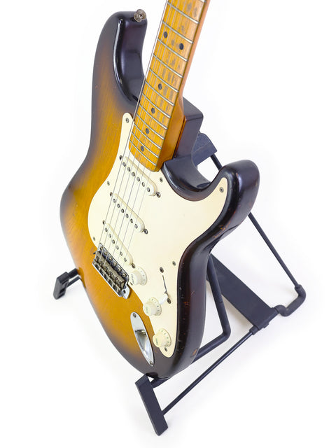Classic 1954 Fender Stratocaster guitar on a stand, highlighted by a simple white background, emphasizing its vintage appeal.