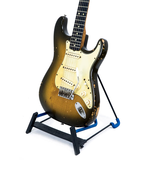 Classic 1963 L Series Stratocaster guitar resting on a stand, set against a dark background.