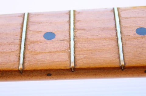 Close-up image of the fretboard from a vintage 1957 Fender Stratocaster, highlighting its Dakota Red refinished surface.
