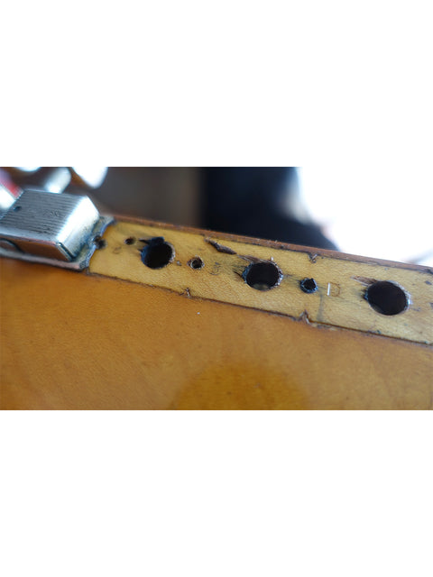 Close-up shot of a vintage 1963 L Series Stratocaster guitar, showcasing holes in its body.