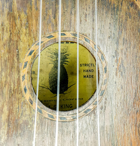 Detailed view of a 1930 Kamaka pineapple ukulele, highlighting its vintage craftsmanship alongside a guitar.