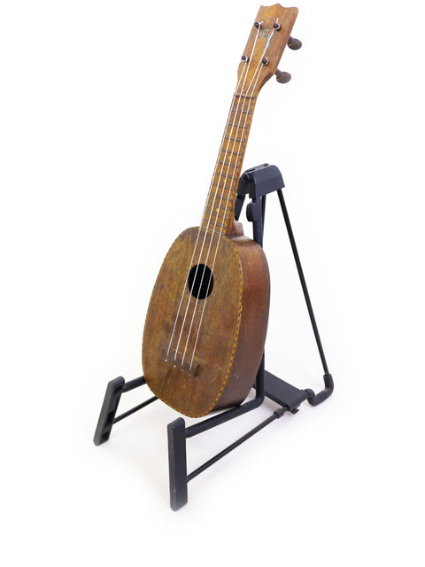 Displaying a 1930 vintage Kamaka Pineapple Ukulele from Hawaii, resting on a stand with charm.