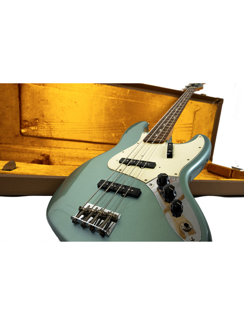 Electric bass guitar lying against an open case on a white background.